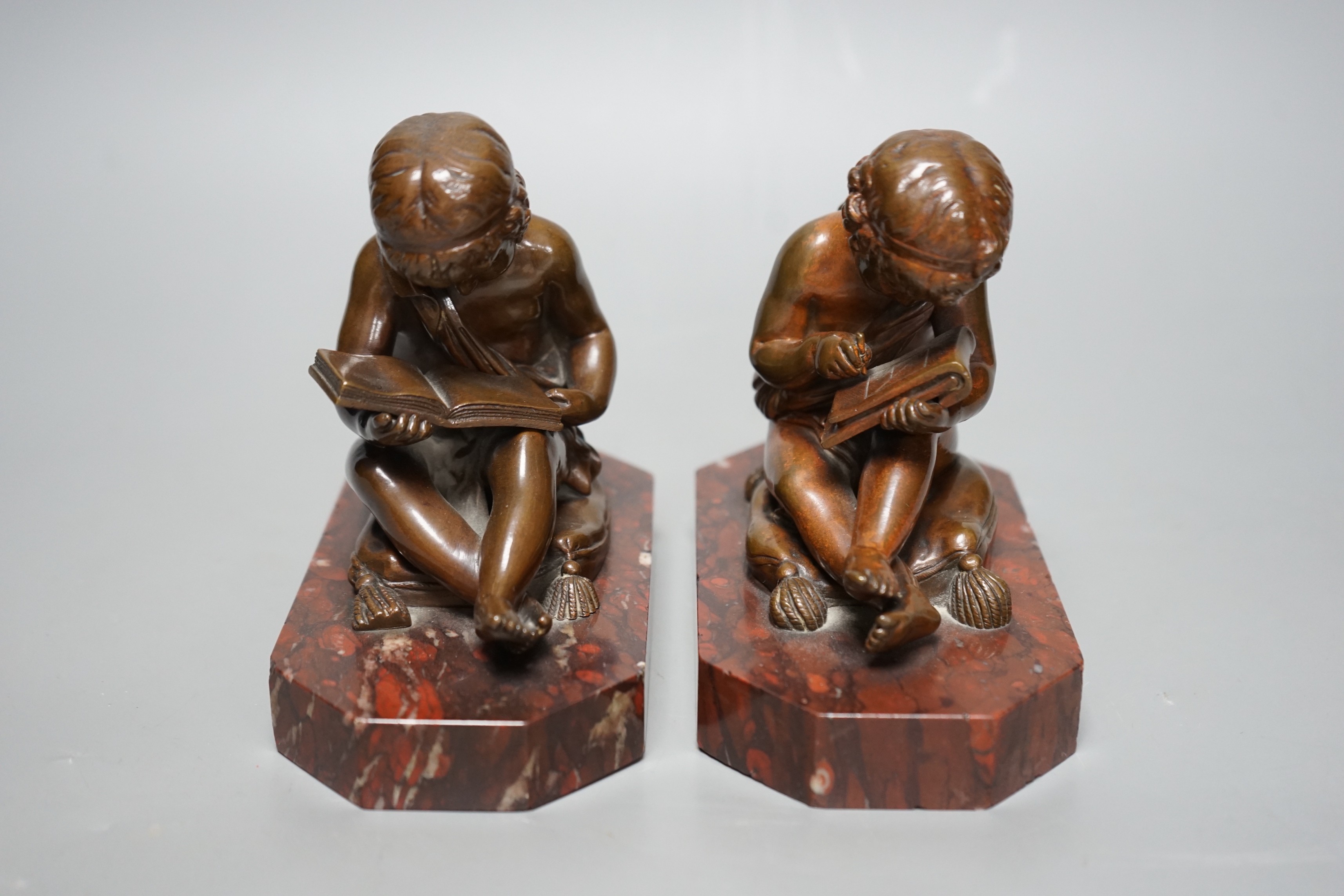 After Charles Gabriel Lemire (1741-1827), a pair of bronze studies of boys seated on cushions, writing and reading, E. Colin & Cie, Paris foundry marks, on rouge marble bases, 14cm long